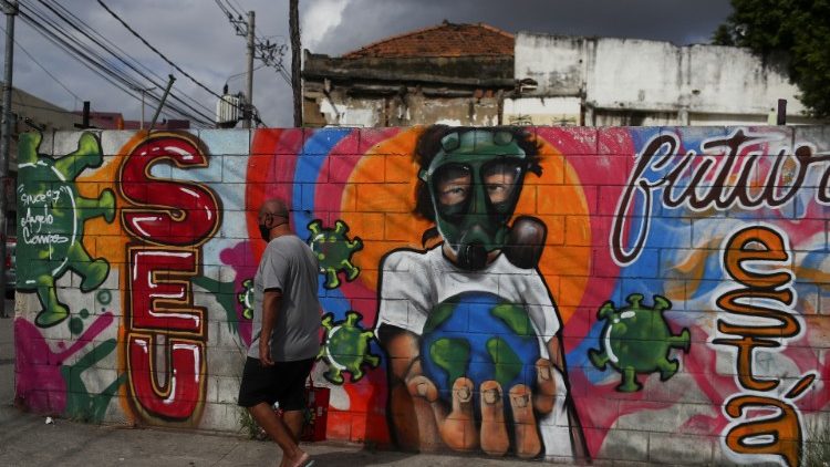 A man walks in front of a graffiti of a boy wearing a face mask in Rio de Janeiro, Brazil