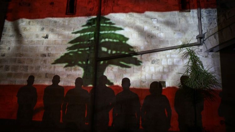 Christian worshippers stand by a wall as a Lebanese national flag is projected on it in solidarity with the Lebanese people following the blast in Beirut, outside a church in Nazareth