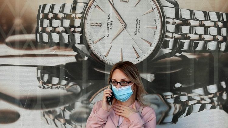 Frau mit Mund-Nasenschutz vor einer Uhrenwerbung 