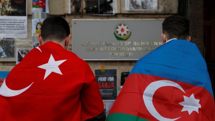 मार्कशिफ्ट मेमोरियल के पास खड़ेअजरबैजैन और तुर्की का झंडा लिए दो व्यक्ति 