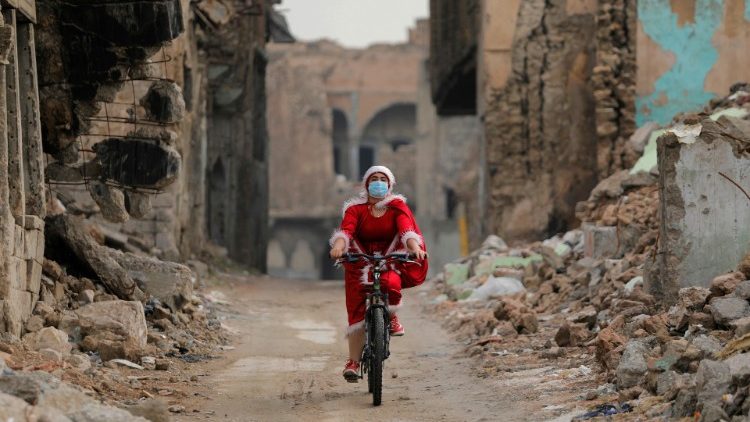 Adventszene in einer zerstörten Straße von Mossul: Irakische Frau im Nikolaus-Kostüm auf dem Fahrrad