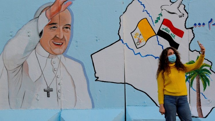 Iraquiana faz um selfiee diante de um mural com o Papa Francisco, na parede de uma igreja em Bagdá