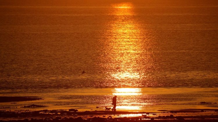 A man walks his dog along the beach as the sun rises at New Brighton