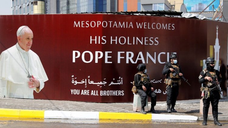 Ozbrojenci před plakátem vítajícím papeže Františka v Bagdádu