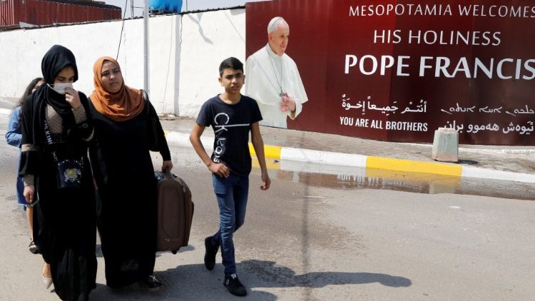 People walk past a poster of Pope Francis ahead of the planned visit of Pope Francis to Iraq, in Baghdad