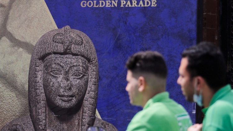 Men pass in front of poster for pharaohs golden parade in Cairo