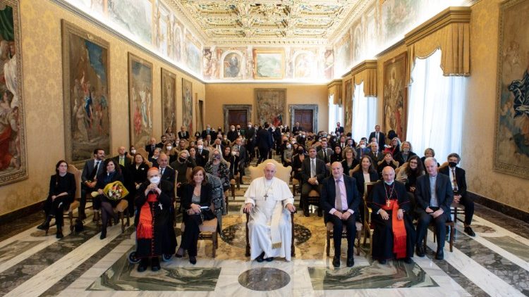 Ferenc pápa a vatikanista újságírókkal, mellette ülnek a díjazottak  