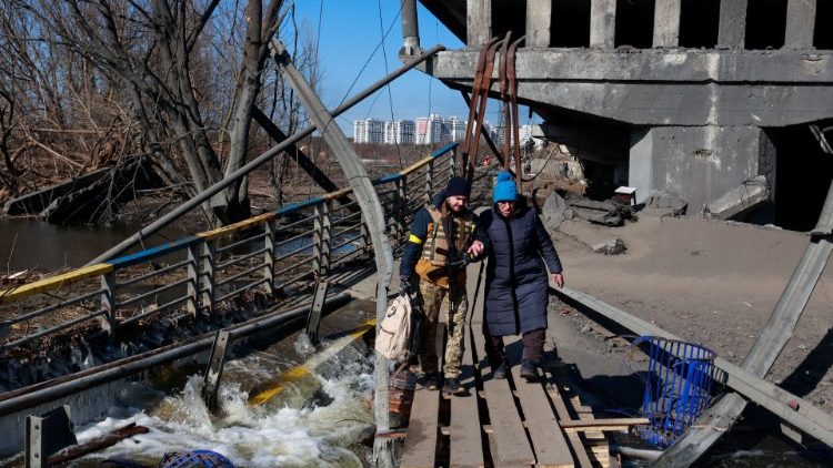 Um membro das forças ucranianas ajuda uma mulher a atravessar o rio Irpin ao lado de uma ponte destruída, em meio à invasão russa da Ucrânia, fora de Kiev, Ucrânia 11 de março de 2022. REUTERS/Serhii Nuzhnenko