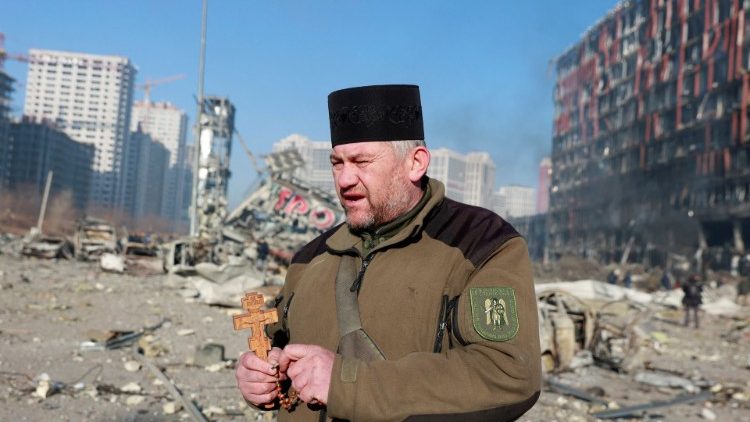 Capelão Mykola Medinsky com um Crucifixo e um Rosário diante de shopping center destruído pelos russo em Kiev, em 21 de março. REUTERS/Serhii Nuzhnenko