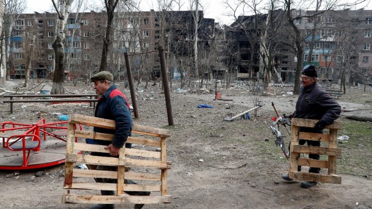 Men carry wooden pallets in the courtyard of an apartment building destroyed in the course of Ukraine-Russia conflict in the besieged southern port city of Mariupol, Ukraine March 25, 2022. REUTERS/Alexander Ermochenko
