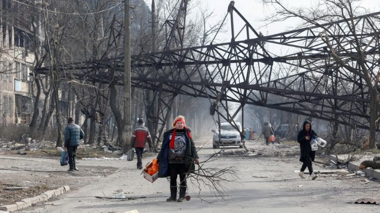 Moradores locais caminham perto de um poste de eletricidade caído e um prédio de apartamentos destruído durante o conflito Ucrânia-Rússia na cidade portuária sitiada de Mariupol, Ucrânia, em 25 de março de 2022 REUTERS/Alexander Ermochenko