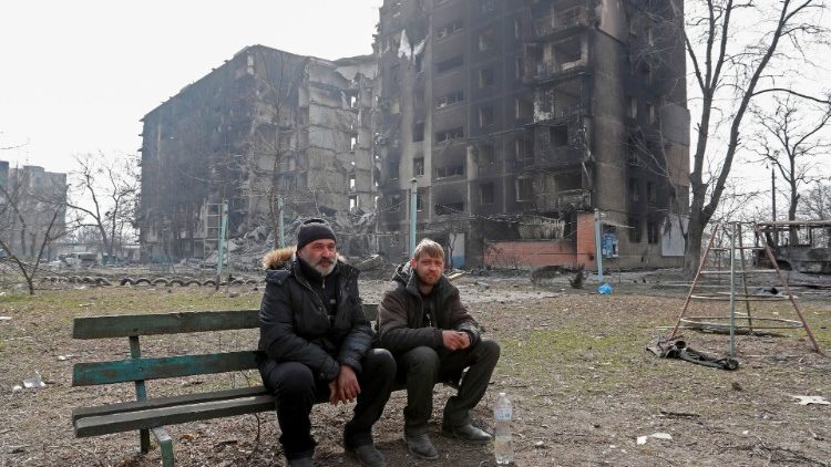 Moradores locais sentam-se em um banco perto de um prédio de apartamentos destruído durante o conflito Ucrânia-Rússia na cidade portuária sitiada de Mariupol, Ucrânia, em 25 de março de 2022 REUTERS/Alexander Ermochenko