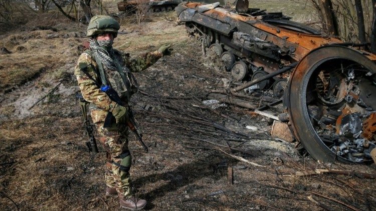 A soldier stands near the wreck of an Armoured Personnel Carrier on the front line in the Kyiv region