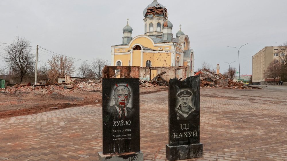 Tombstones with portraits of Russian president Putin and Belarus President Lukashenko are seen in front of a church damaged by shelling in Malyn