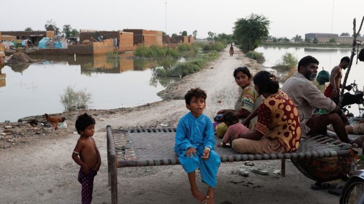 Vítimas de enchentes, uma família, sentam-se ao longo de uma rua com as casas submersas ao fundo, após chuvas e inundações durante a estação das monções em Mehar, Paquistão, 29 de agosto de 2022. REUTERS/Akhtar Soomro