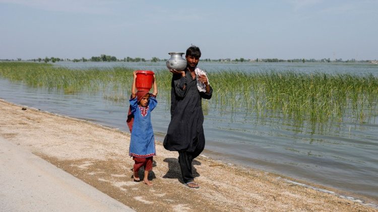 Um homem e uma menina carregam panelas enquanto caminham ao lado de campos inundados, após chuvas e inundações durante a estação das monções em Mehar, Paquistão, 31 de agosto de 2022. REUTERS/Akhtar Soomro