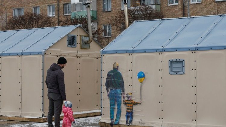 Um homem com uma criança olha uma obra de arte do famoso artista de rua Tvboy, criada na parede de um 'centro de invencibilidade', em meio ao ataque da Rússia à Ucrânia, na cidade de Bucha, nos arredores de Kyiv, Ucrânia, 29 de janeiro de 2023. REUTERS/Valentyn Ogirenko