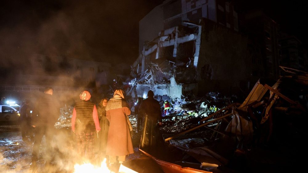Pessoas olham para um prdio desabado enquanto se renem em torno de uma fogueira, aps um terremoto em Iskenderun, Turquia, 6 de fevereiro de 2023. REUTERS/Umit Bektas