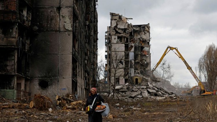 A woman reacts as she walks through her neighbourhood past destroyed apartment blocks in Mariupol