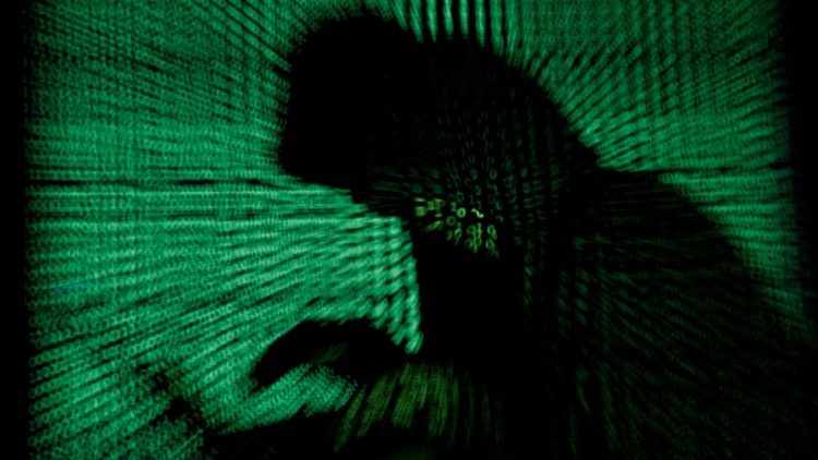 Un homme encagoulé tient un ordinateur portable alors qu'un cybercode est projeté sur cette photo d'illustration.