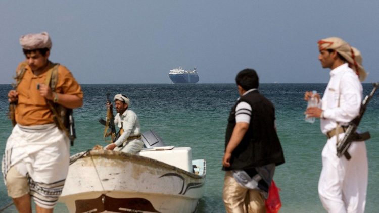Uomini armati in piedi sulla spiaggia mentre la nave commerciale Galaxy Leader, sequestrata dagli Houthi dello Yemen il mese scorso,  ancorata al largo della costa di al-Salif