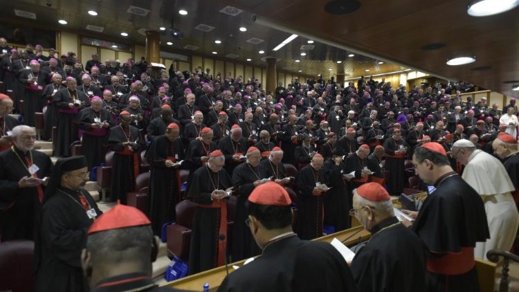 Papež Frančišek in škofje ter kardinali med molitvijo v sinodalni dvorani.