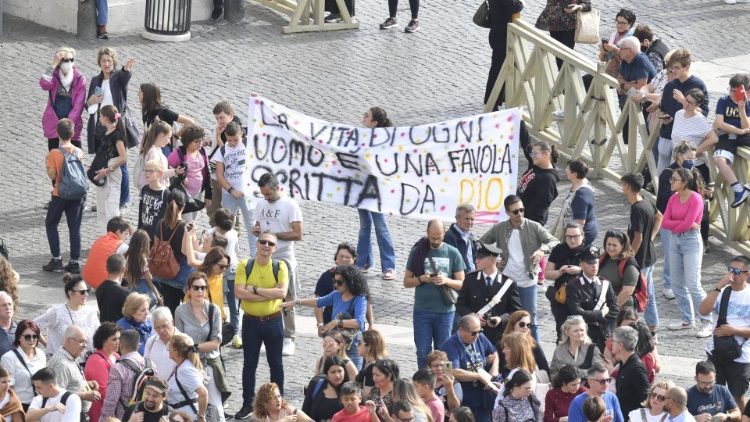 Fiéis na Praça São Pedro seguram faixa com os dizeres: "A vida de cada homem é uma fábula escrita por Deus"