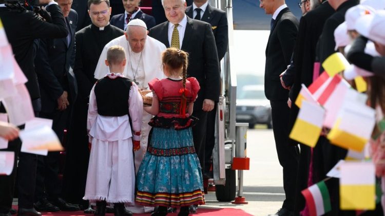 O Papa sendo acolhido no Aeroporto de Budapeste por um casal de crian?as vestindo trajes tpicos locais