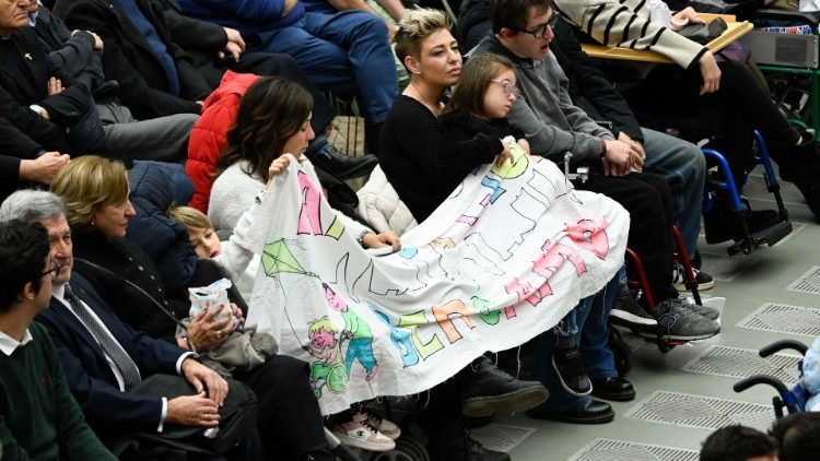 Uno striscione sulle ginocchia di persone malate e disabili in Aula Paolo VI