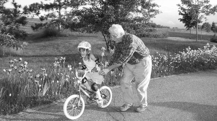 Un grand-père apprenant à sa petite-fille à faire du vélo.