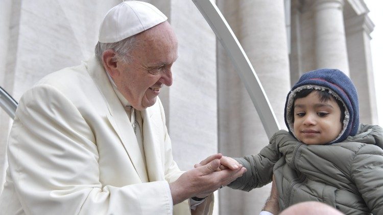 Pope Francis takes the hand of a child at his general audience.