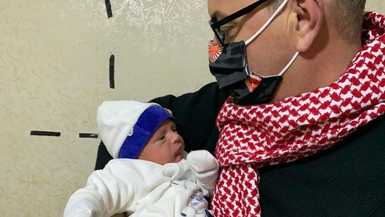 Don Mario con in braccio il neonato Mario, figlio di una coppia di profughi iracheni accolti in Giordania