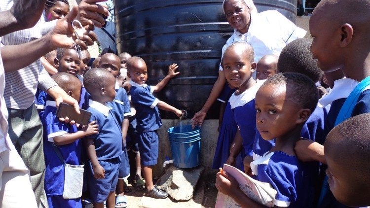 Sr. Bokamba with local schoolchildren at one of the water tanks