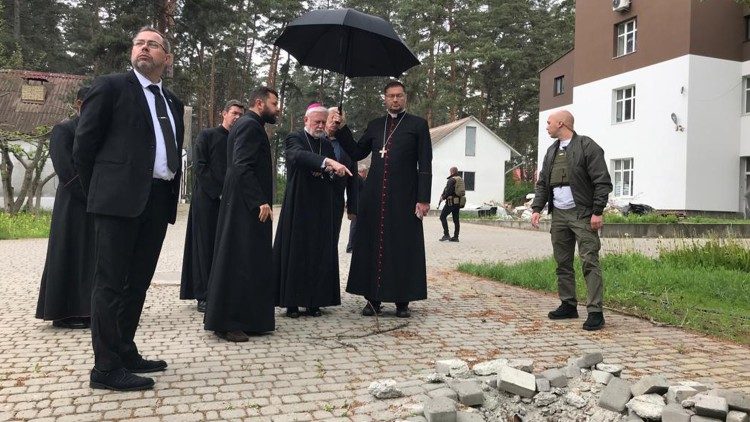 L'arcivescovo Gallagher, il nunzio Kulbokas e il direttore del Seminario romano cattolico di Vorzel davanti al cratere scavato da un missile Grad
