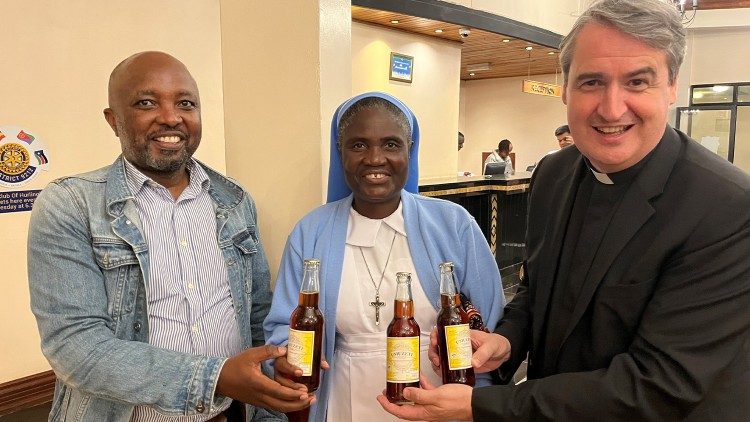 A Irmã Mary Chilengwe das Irmãs do Menino Jesus mostra o vinho de abacaxi produzido pelas Pequenas Serva de Maria em Ruanda. Também estão na foto o gerente de investimentos do país, Geoffrey Ndashimye, e o padre Andrew Small